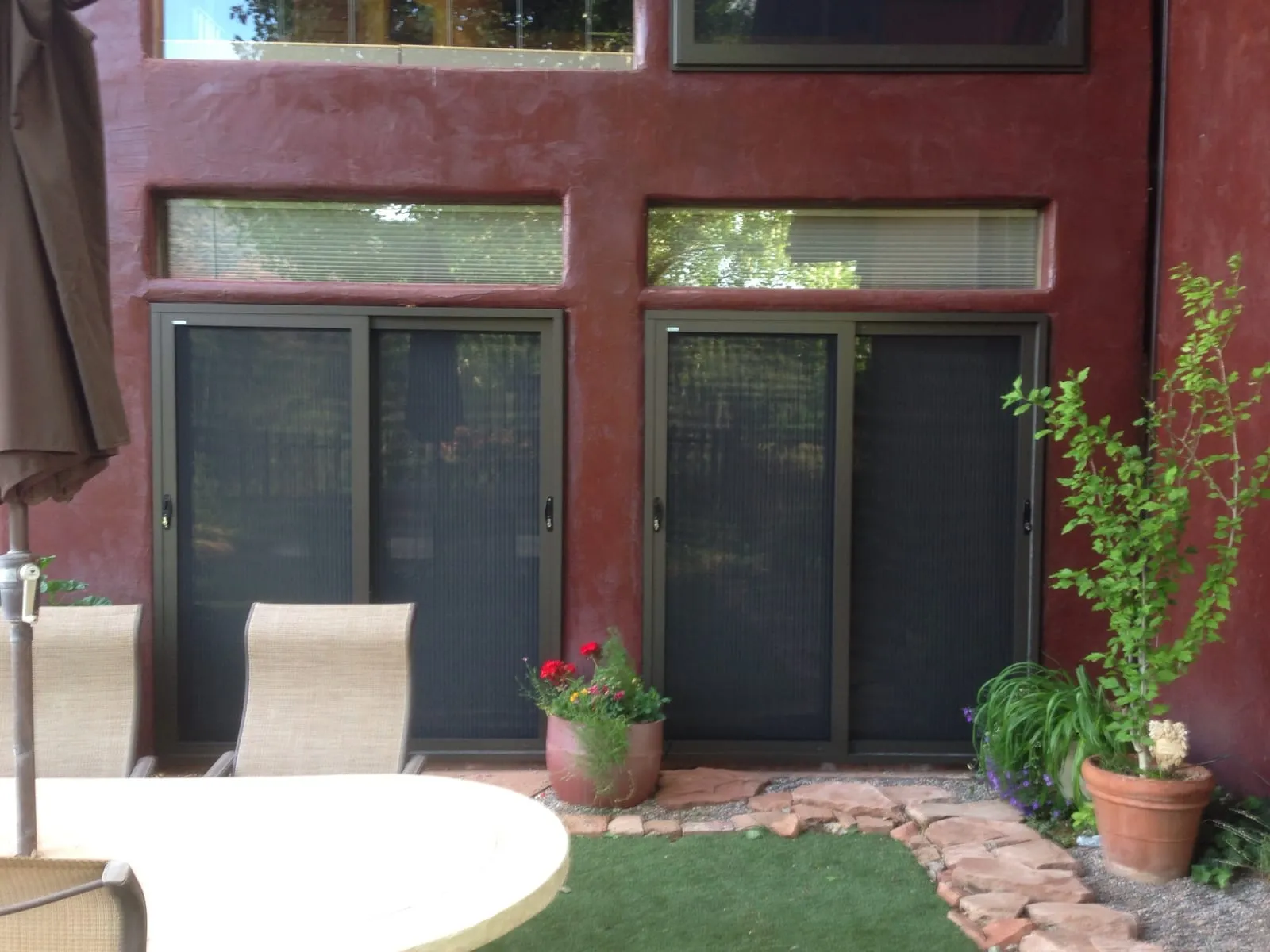 Two bronze sliding security screen doors on a deep-red stucco patio wall